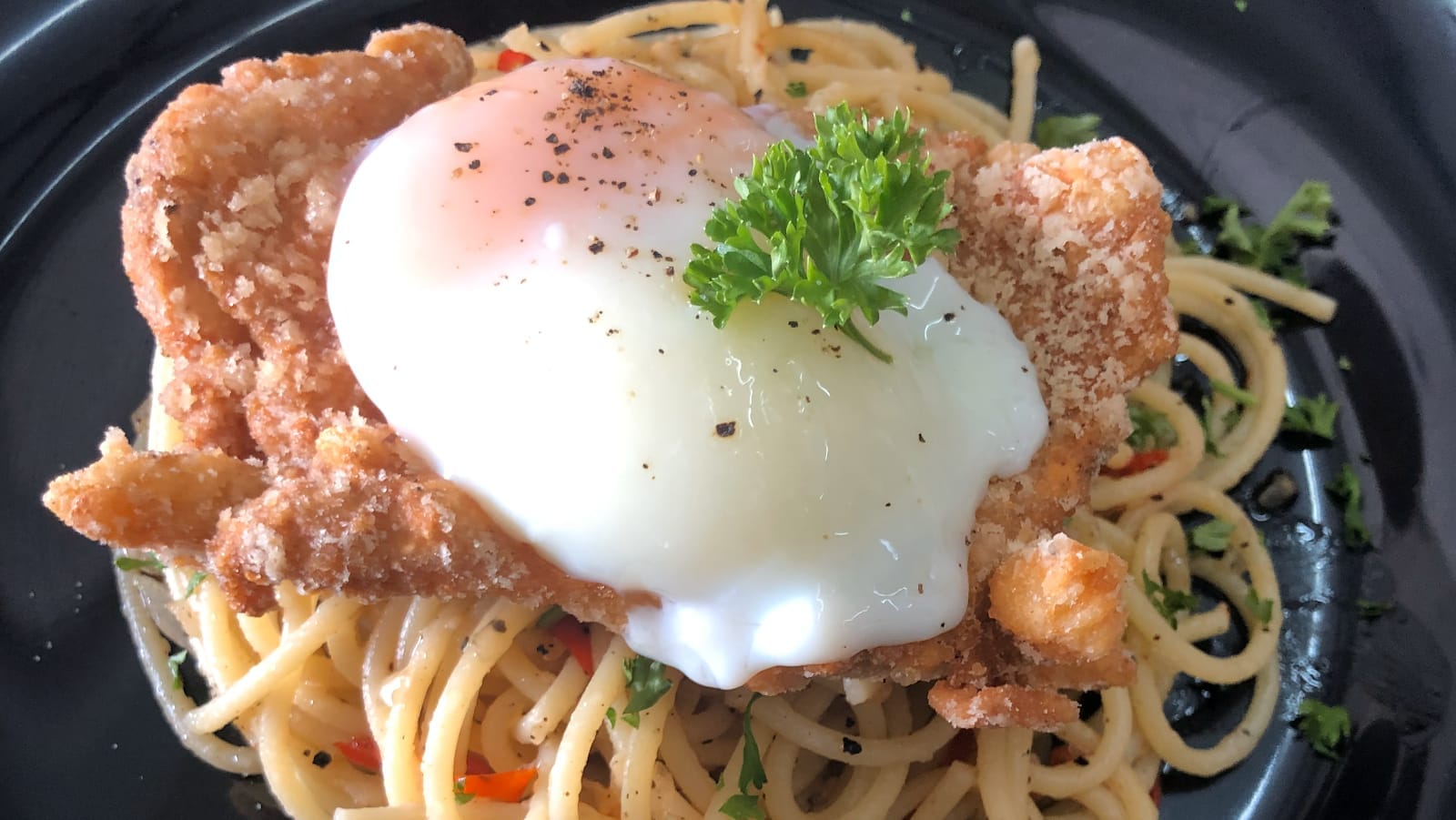 Chicken chop aglio-olio: a fried chicken chop topped with a soft egg on garlic and chilli spaghetti, in a black bowl