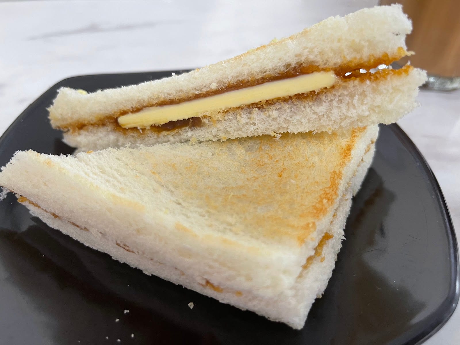 Toast cut into triangles with kaya and a slab of butter, on a black plate